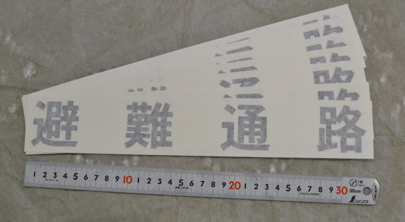 マンションベランダの仕切り板に避難通路の文字をカッティングシートで表示